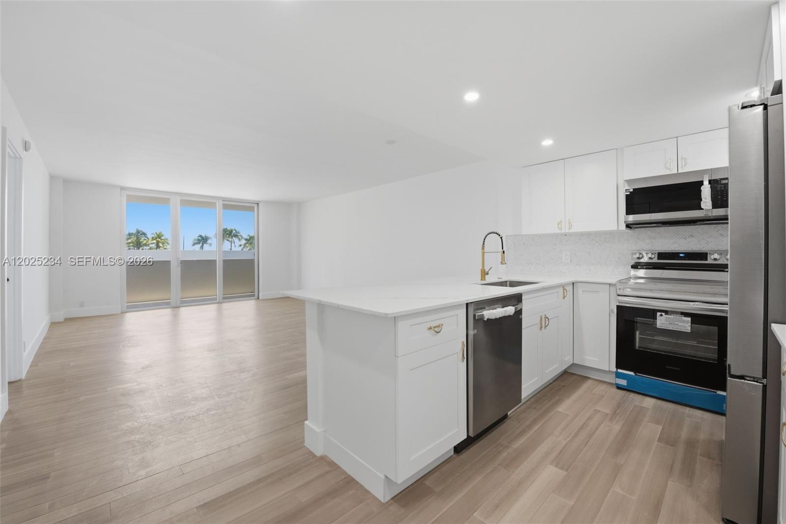 A modern kitchen with white cabinets and stainless steel appliances opens to a living area — 5 Island Ave # 2F, Miami Beach FL 33139, MIAMI BEACH, FL