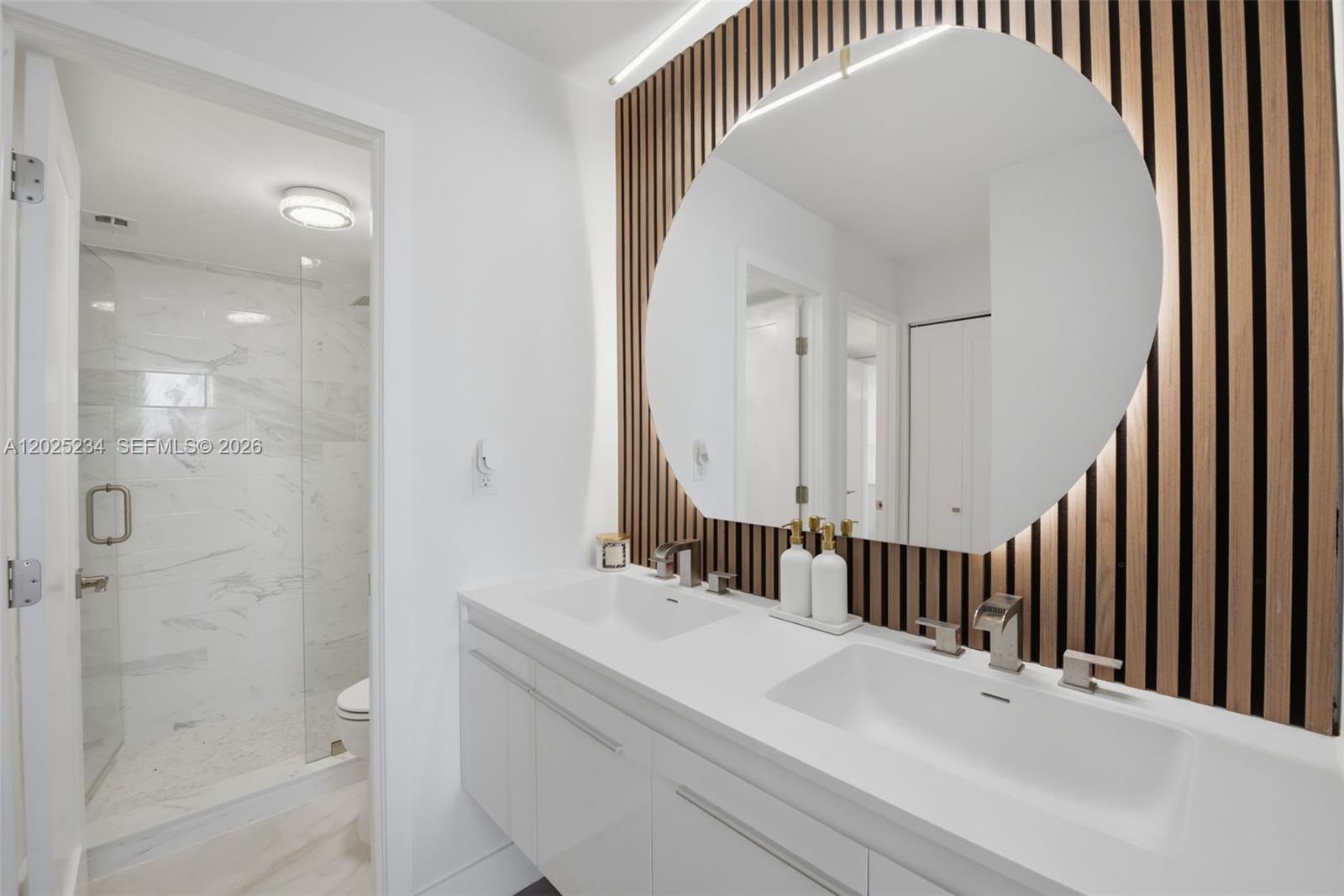 A modern bathroom features a double vanity, a large circular mirror, and a glass-enclosed shower — 5 Island Ave # 2F, Miami Beach FL 33139, MIAMI BEACH, FL