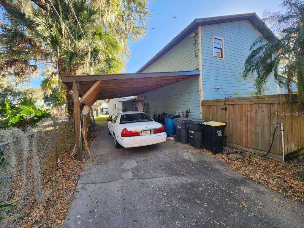 A white sedan is parked under a wooden carport next to a light blue house — 9428 CAT TRACK TRAIL, LAKE WALES, FL