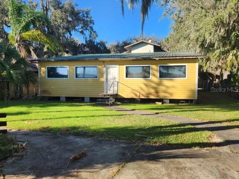 A yellow, single-story house with a metal roof stands on concrete piers in a yard — 9428 CAT TRACK TRAIL, LAKE WALES, FL