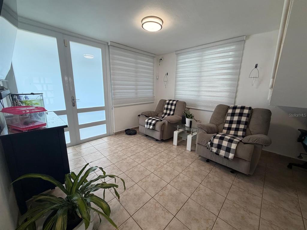 A sunroom features tile flooring, two gray armchairs with plaid throws, and large windows — A18 CALLE RIO FAJARDO, LUQUILLO, PR