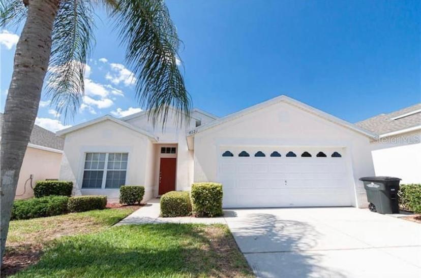 A single-story house with a white exterior, a red front door, and a two-car garage — 8121 FAN PALM WAY, KISSIMMEE, FL