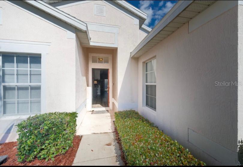 A view of a home entrance with a concrete walkway, bushes, and an open door — 8121 FAN PALM WAY, KISSIMMEE, FL