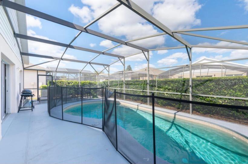 A swimming pool enclosed by a screened lanai with a black safety fence — 8121 FAN PALM WAY, KISSIMMEE, FL