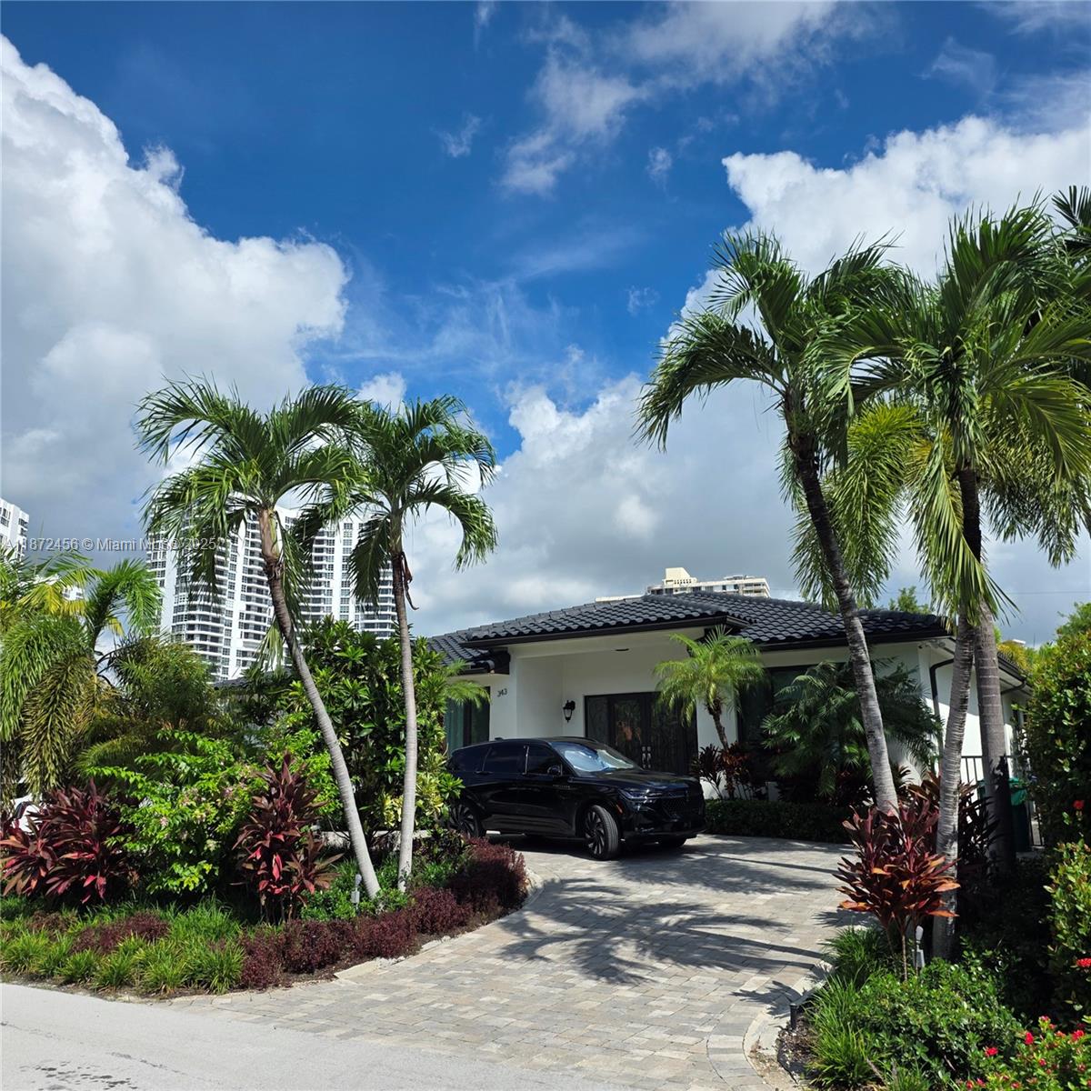 A black SUV is parked in the driveway of a single-story house with palm trees — 343 190th St, Sunny Isles Beach FL 33160, SUNNY ISLES BEACH, FL