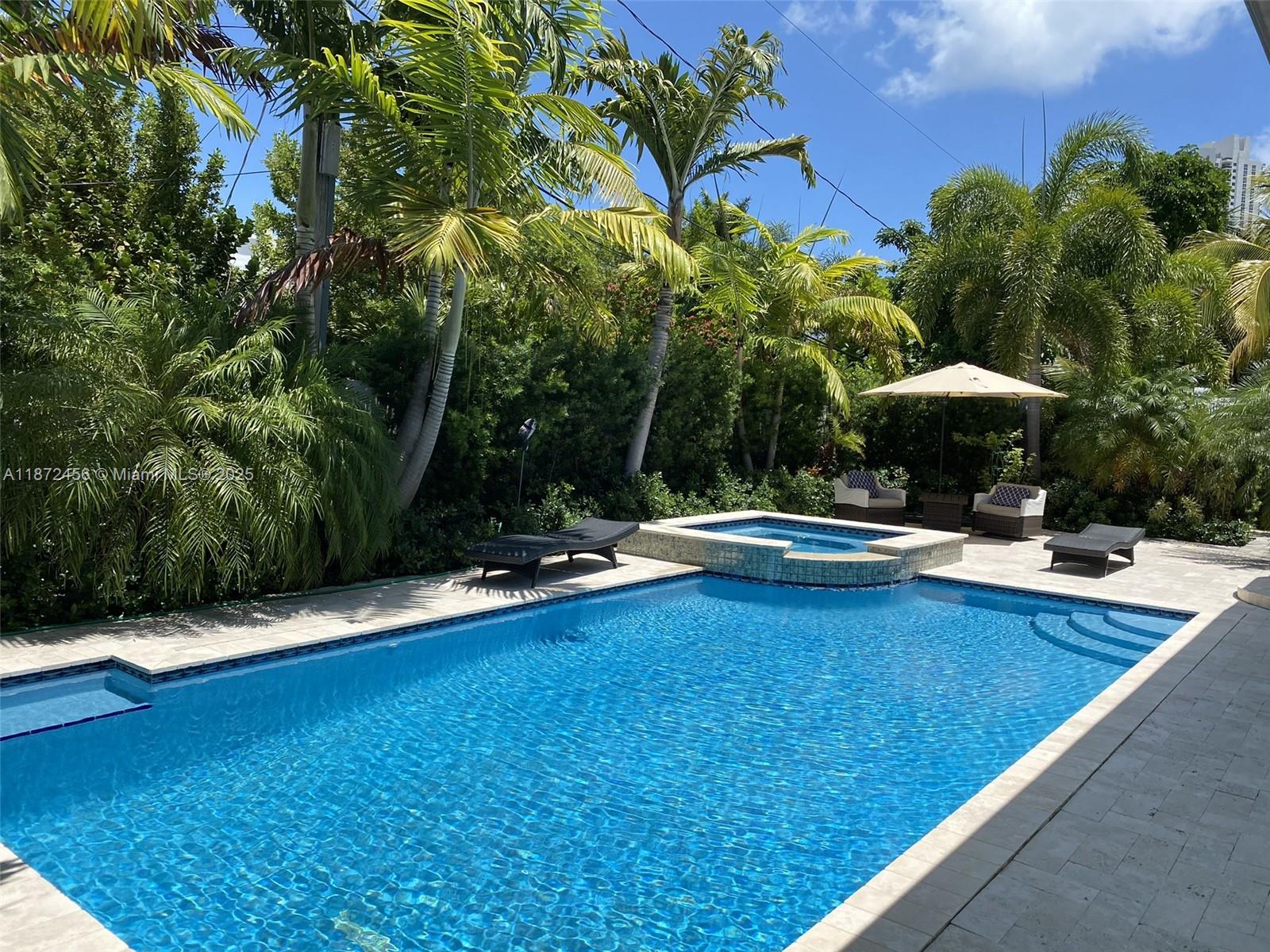 A backyard features a rectangular swimming pool with an attached spa, lounge chairs, and palm trees — 343 190th St, Sunny Isles Beach FL 33160, SUNNY ISLES BEACH, FL