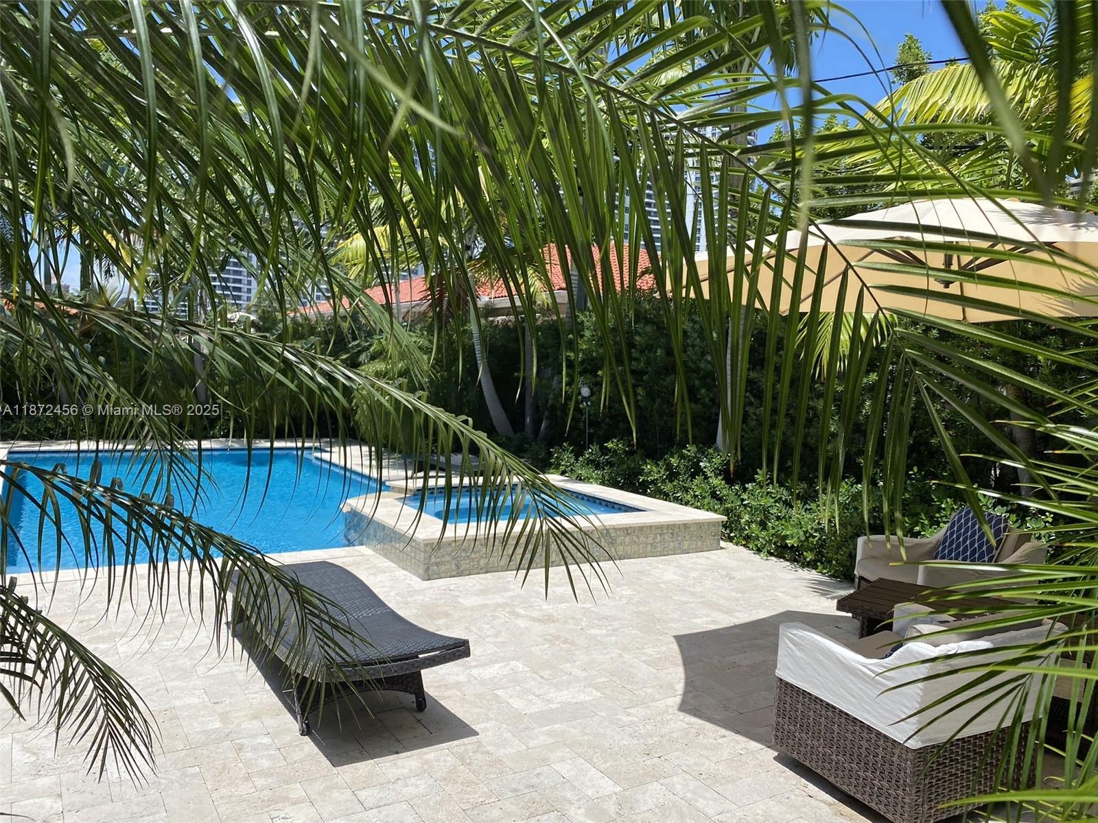 A backyard patio features a swimming pool, a spa, lounge chairs, and palm trees — 343 190th St, Sunny Isles Beach FL 33160, SUNNY ISLES BEACH, FL