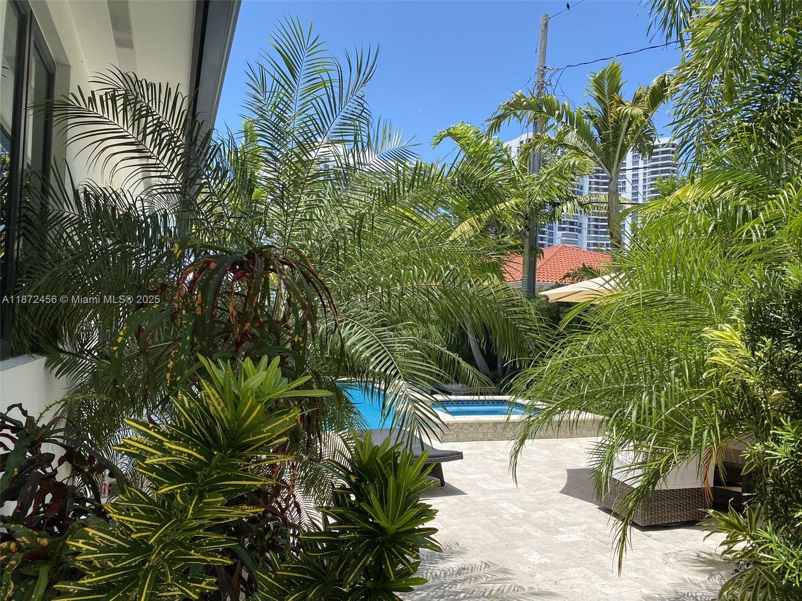 A backyard patio features a swimming pool, lounge chairs, and lush tropical landscaping — 343 190th St, Sunny Isles Beach FL 33160, SUNNY ISLES BEACH, FL