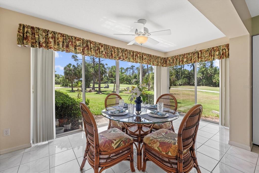 A sunroom with a glass dining table, wicker chairs, tile floors, and golf course views — 813 MONTROSE DRIVE UNIT 102, VENICE, FL