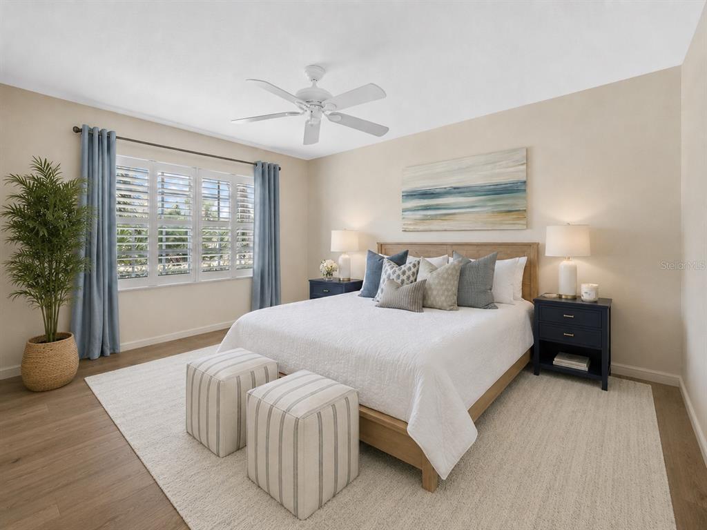 A bedroom features a bed with blue nightstands, a ceiling fan, and a large window — 813 MONTROSE DRIVE UNIT 102, VENICE, FL