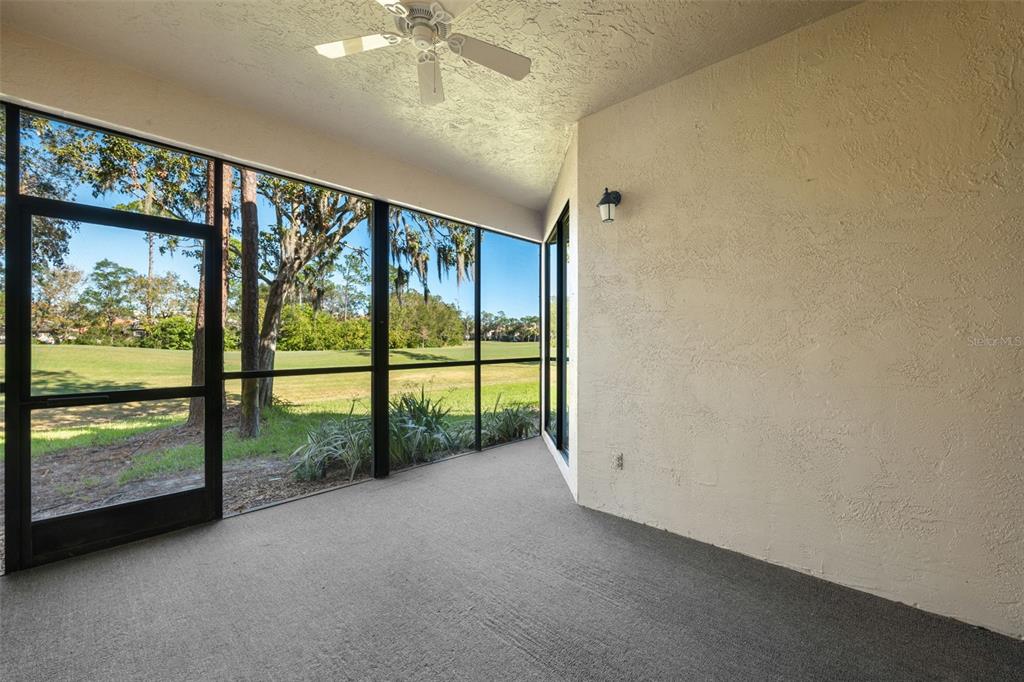 A screened-in porch with a ceiling fan, gray carpet, and views of a grassy field — 121 LINDSAY LANE UNIT 31, OLDSMAR, FL