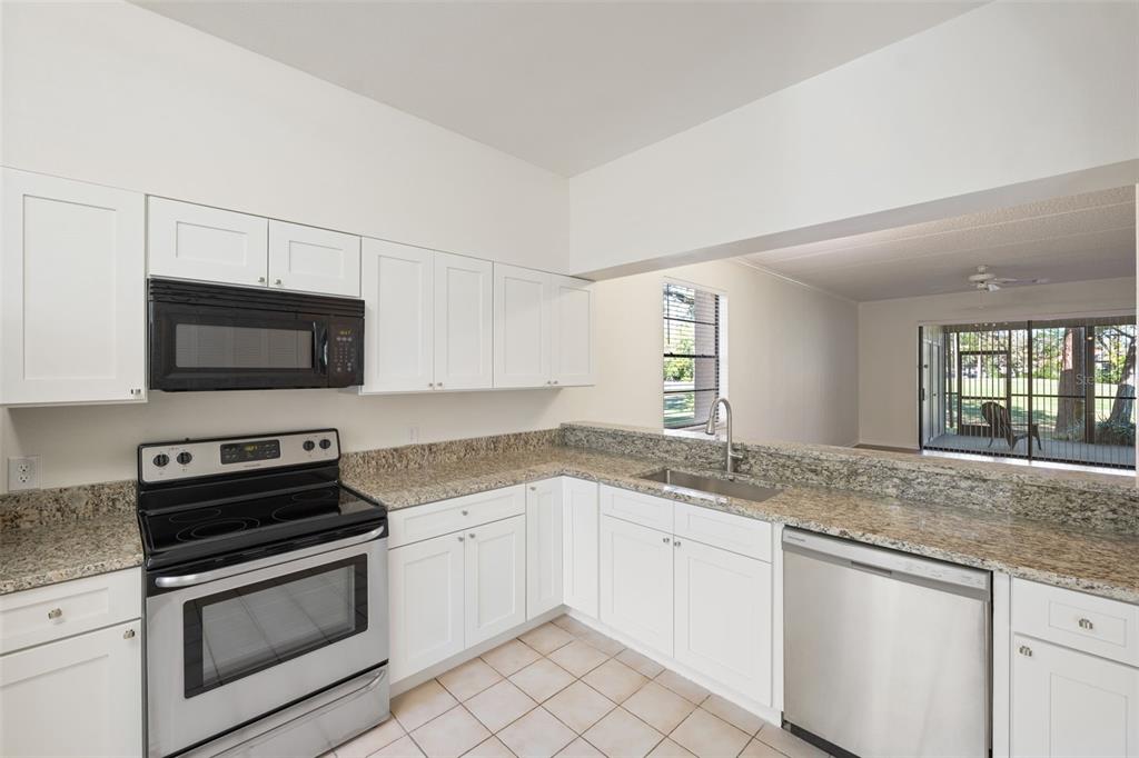 A kitchen features white cabinets, granite countertops, stainless steel appliances, and a view of a patio — 121 LINDSAY LANE UNIT 31, OLDSMAR, FL