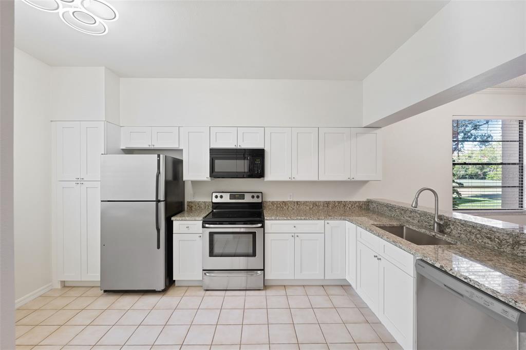 A kitchen with white cabinets, stainless steel appliances, granite countertops, and light-colored tile flooring — 121 LINDSAY LANE UNIT 31, OLDSMAR, FL