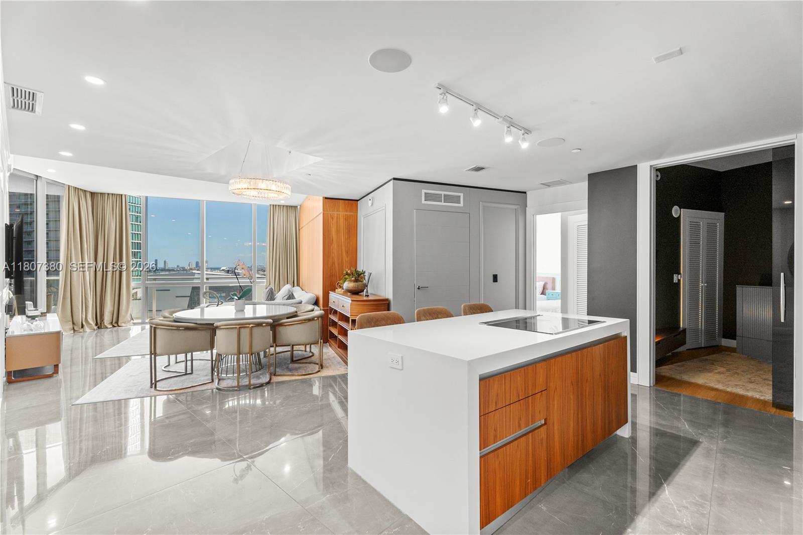 A modern kitchen with a white island and wood cabinetry opens to a dining area — 851 NE 1st Ave # 1409, Miami FL 33132, MIAMI, FL