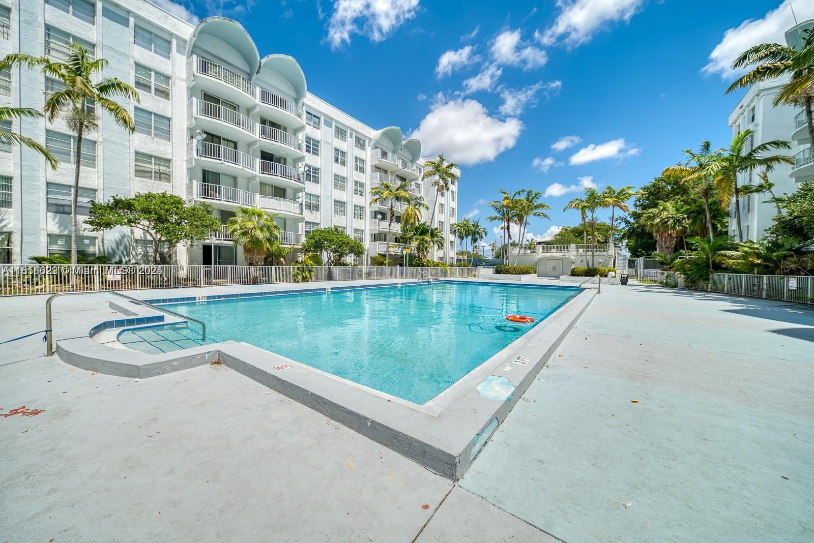 A rectangular swimming pool sits in front of a multi-story white apartment building — 486 NW 165th St Rd # 303, Miami FL 33169, MIAMI, FL