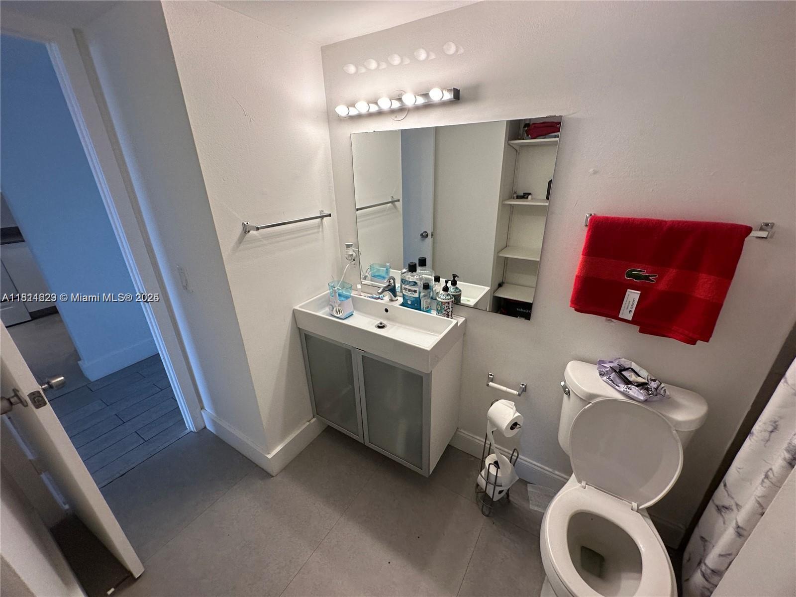 A bathroom features a white vanity, a wall-mounted mirror, a toilet, and a red towel — 486 NW 165th St Rd # 303, Miami FL 33169, MIAMI, FL