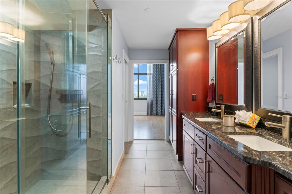 A bathroom features a glass-enclosed shower, dark wood cabinetry, granite countertops, and a doorway view — 1108 N FRANKLIN STREET UNIT 707, TAMPA, FL