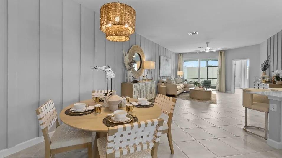 A dining area with a round table and woven chairs sits before an open living room — 8462 WATER LILY COURT, ENGLEWOOD, FL