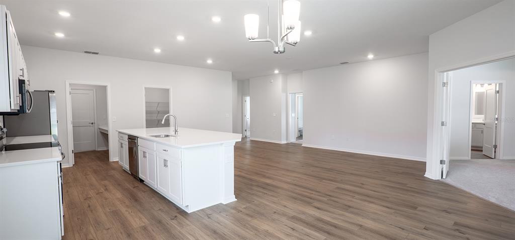 A kitchen with a white island and light wood flooring opens into a spacious living area — 1536 OTTER WOODS LANE, AUBURNDALE, FL