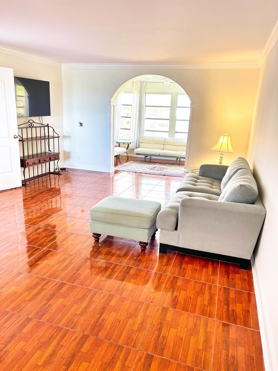 A living room features glossy wood-look tile floors, a gray sofa, and an arched entryway — 14671 Bonaire Boulevard Apt 505, Delray Beach FL 33446, DELRAY BEACH, FL