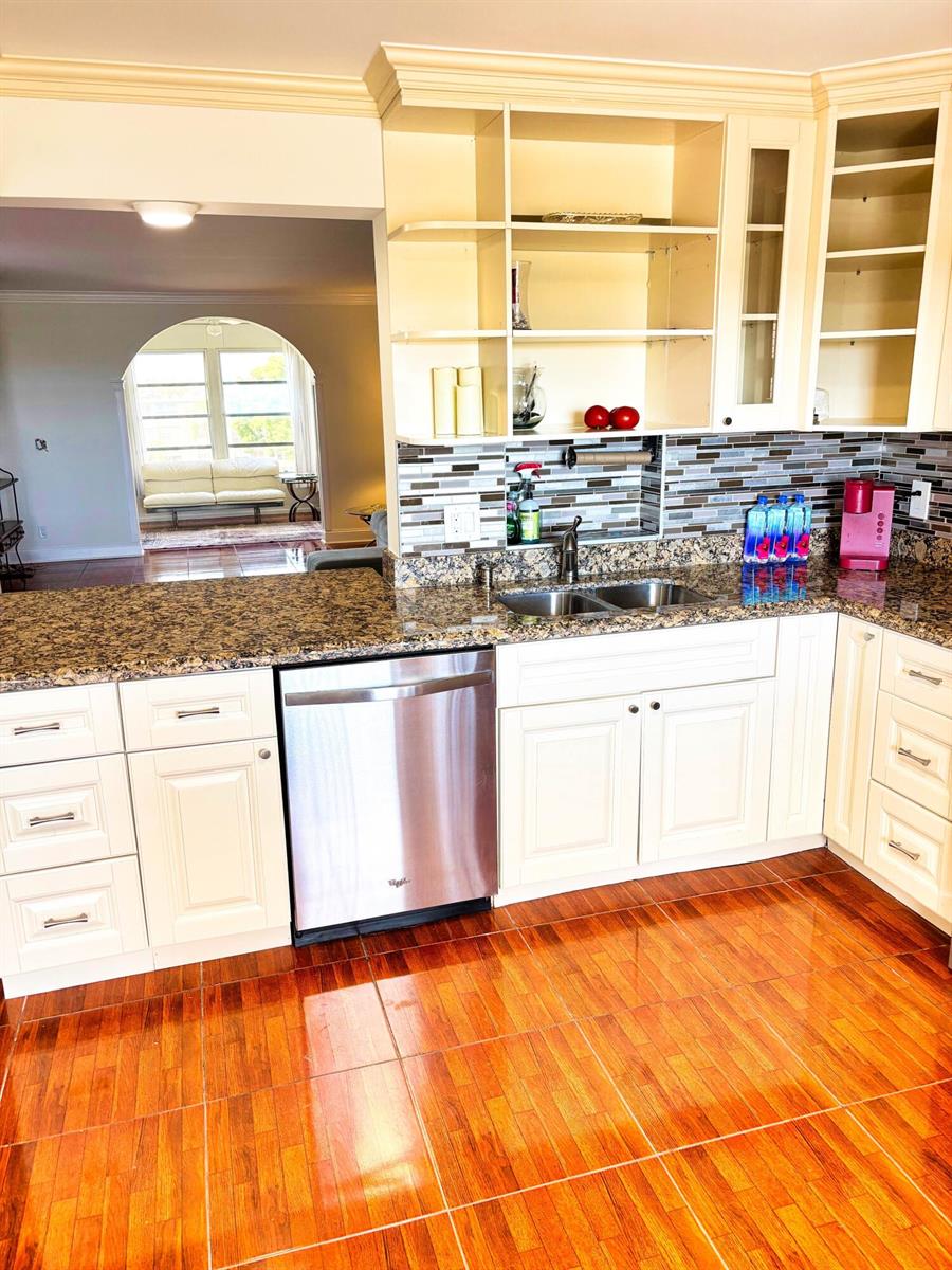 A kitchen features white cabinets, granite countertops, a stainless steel dishwasher, and wood-look tile flooring — 14671 Bonaire Boulevard Apt 505, Delray Beach FL 33446, DELRAY BEACH, FL