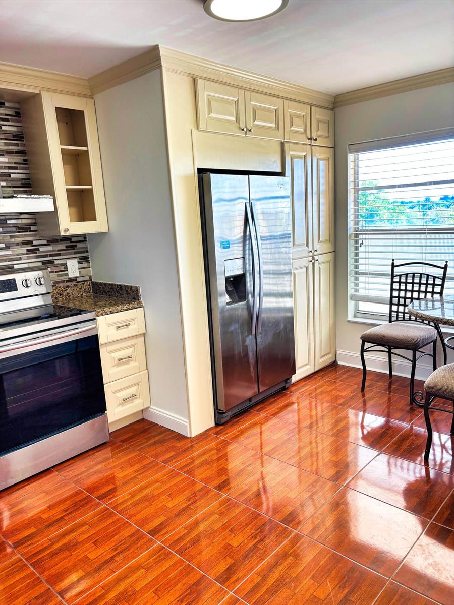A kitchen features cream-colored cabinetry, stainless steel appliances, a tiled backsplash, and glossy wood-look flooring — 14671 Bonaire Boulevard Apt 505, Delray Beach FL 33446, DELRAY BEACH, FL