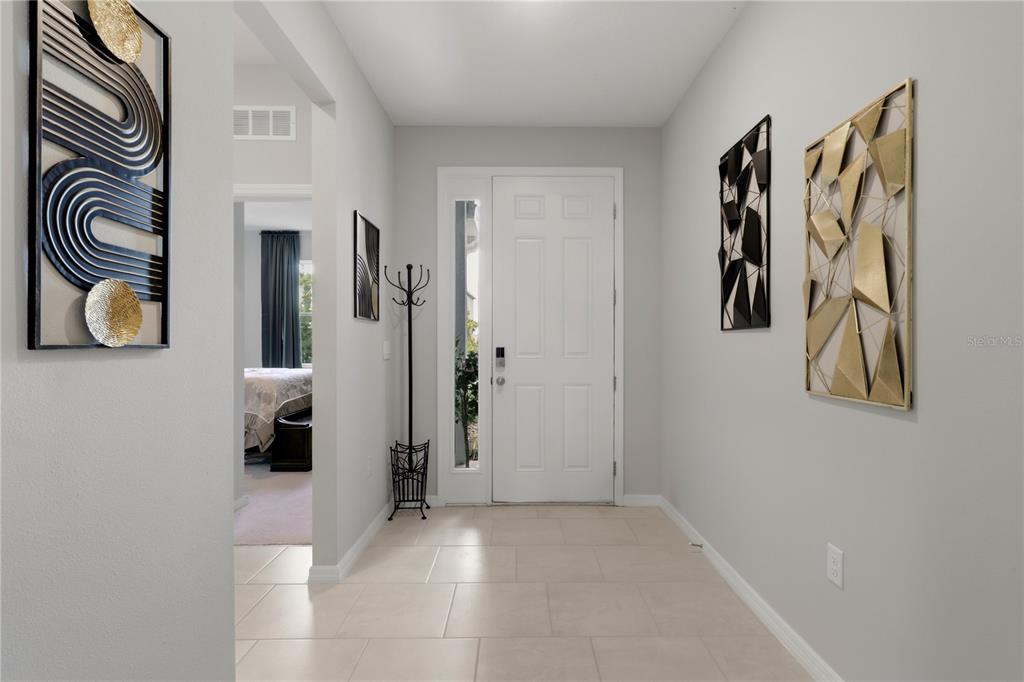 A bright entryway features light tile flooring, a white front door, and decorative wall art — 11316 SPOONBILL FLOCK WAY, SAN ANTONIO, FL