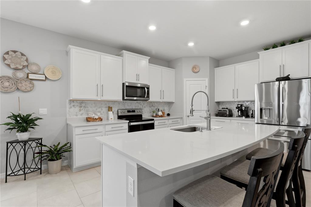 A modern kitchen features white cabinetry, a large quartz island, and stainless steel appliances — 11316 SPOONBILL FLOCK WAY, SAN ANTONIO, FL