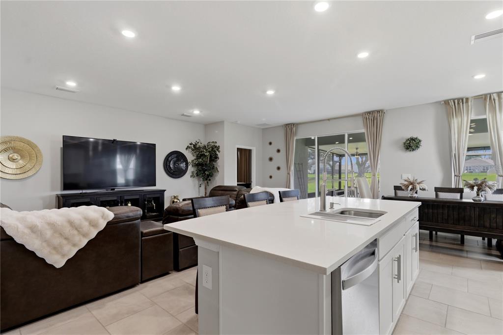 A kitchen island with a sink sits in the foreground of an open-concept living area — 11316 SPOONBILL FLOCK WAY, SAN ANTONIO, FL