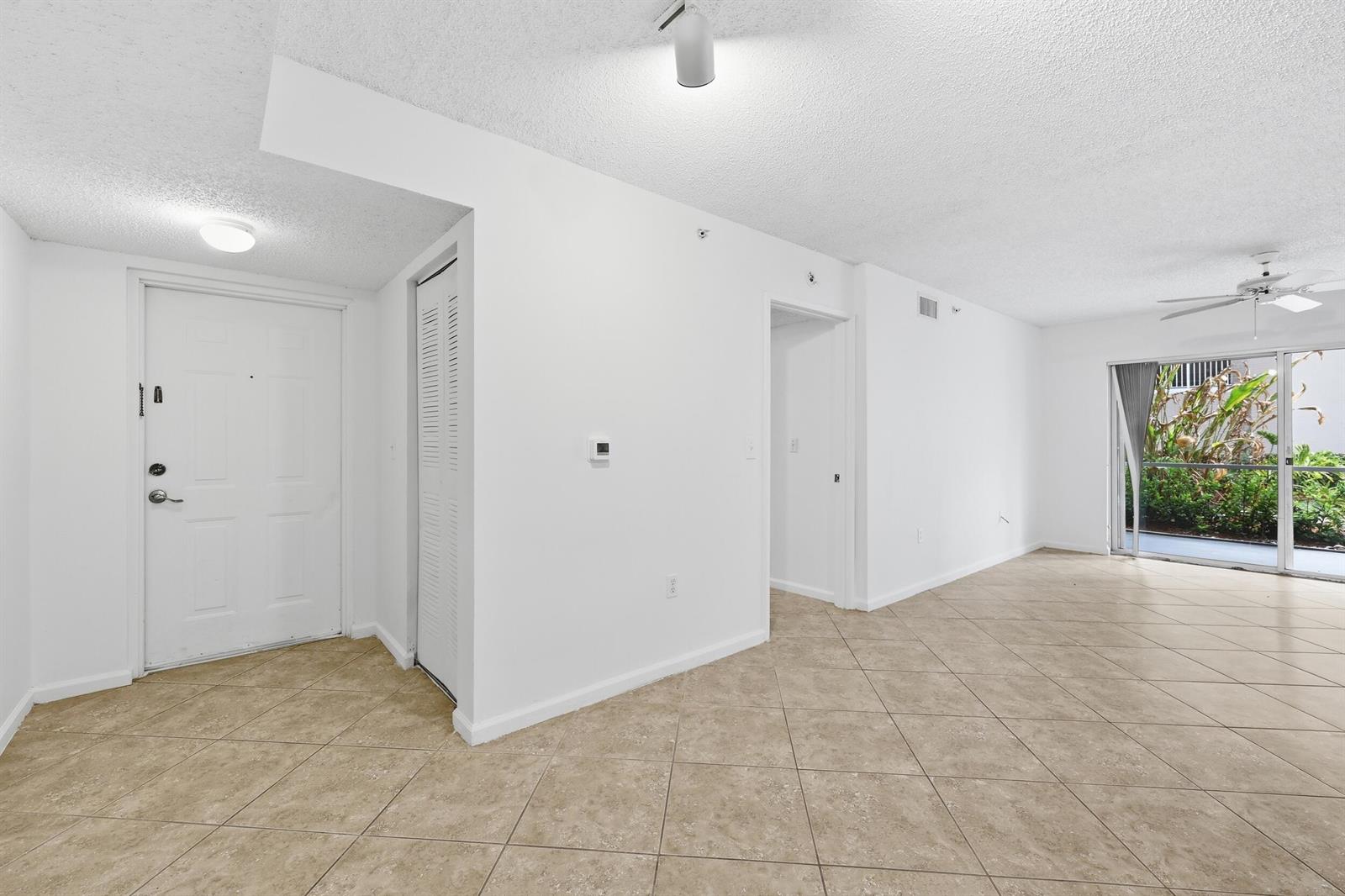 An interior view of a tiled living area with a white front door and patio — 278 Village Boulevard # 8106, Tequesta FL 33469, TEQUESTA, FL