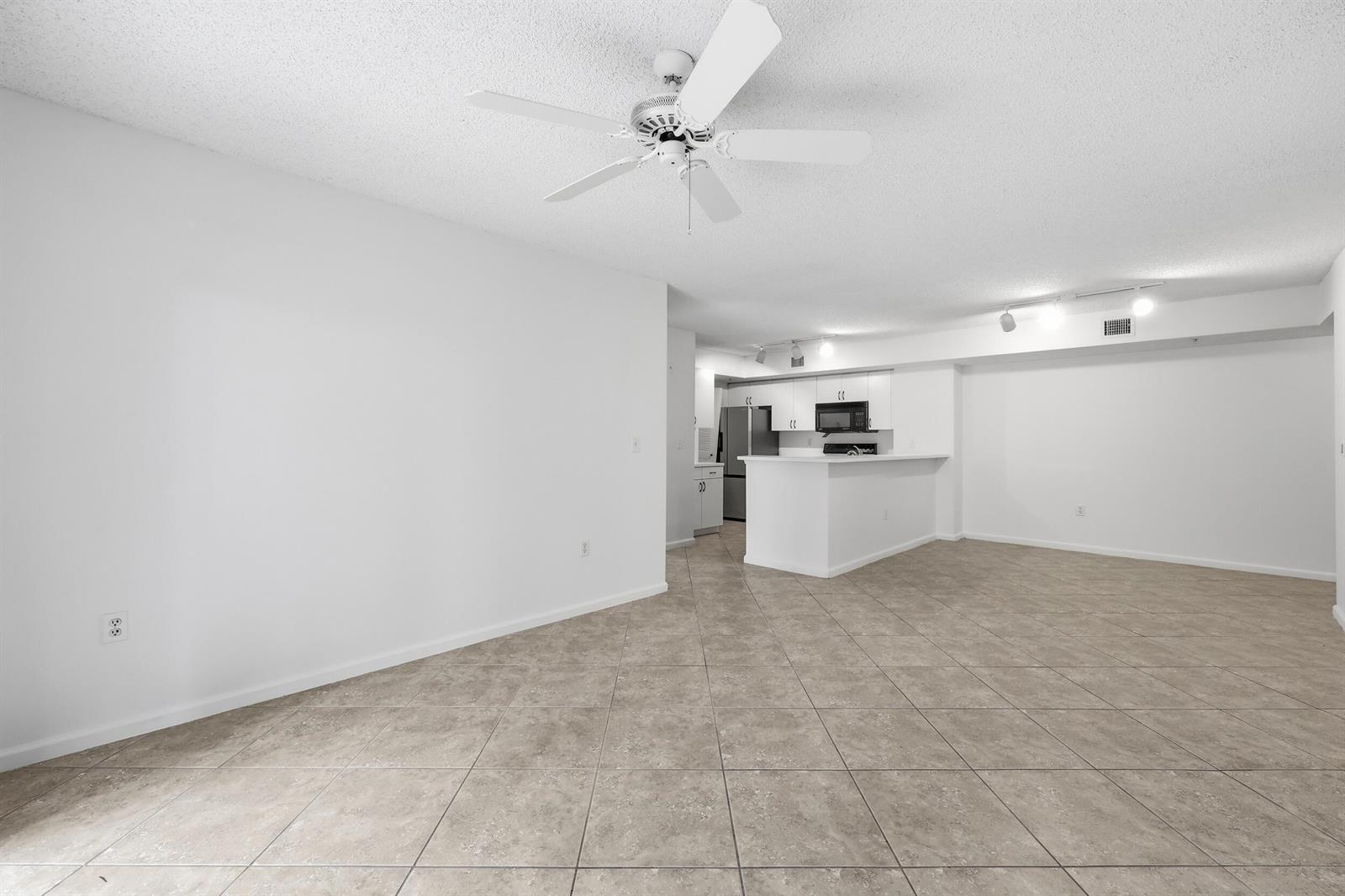 An open-concept living area with tile flooring, a ceiling fan, and a kitchen with white cabinets — 278 Village Boulevard # 8106, Tequesta FL 33469, TEQUESTA, FL