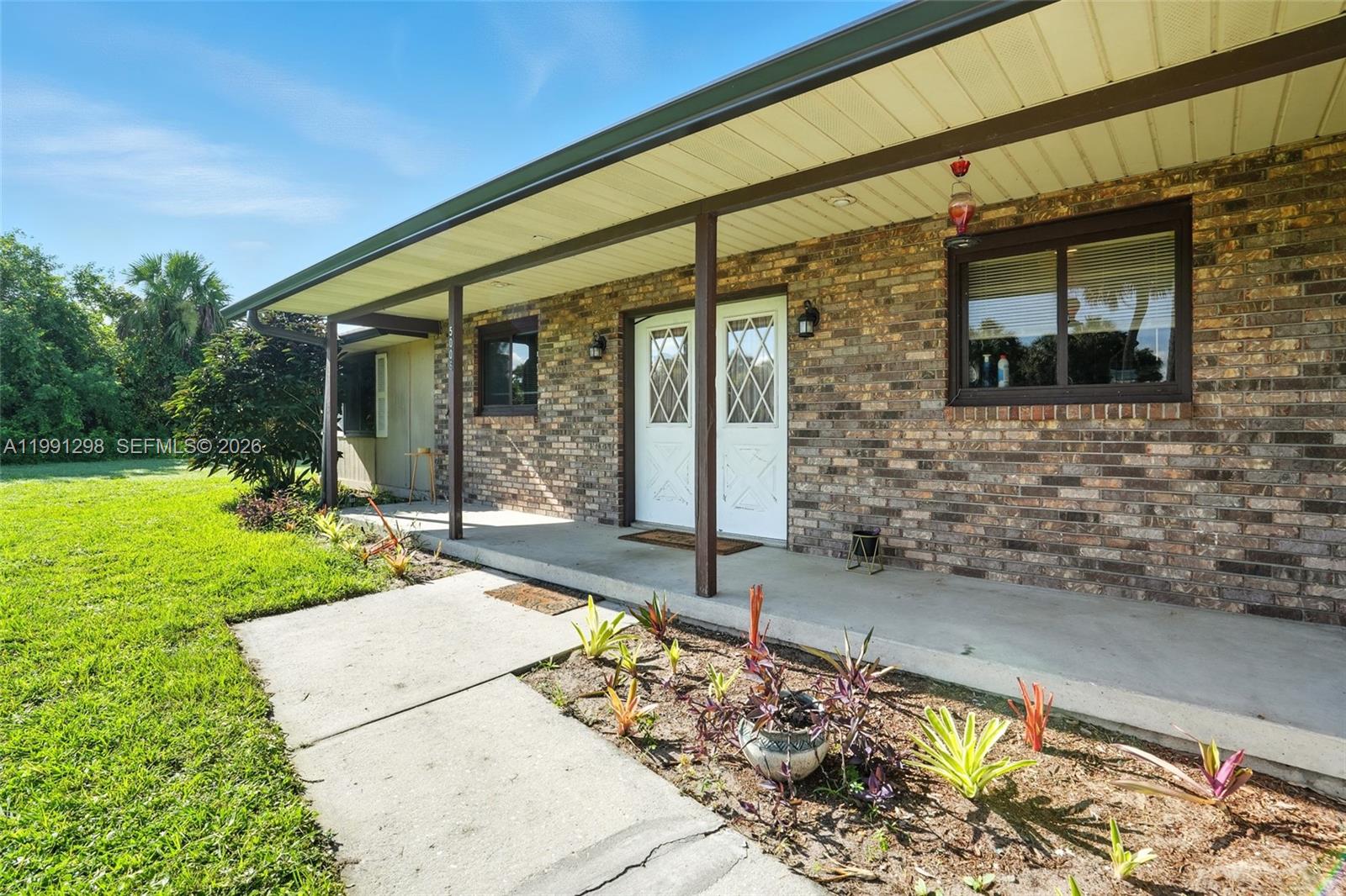 A brick house exterior features a covered porch, white double doors, and a front lawn — 5006 pike ln, La Belle FL 33935, LA BELLE, FL