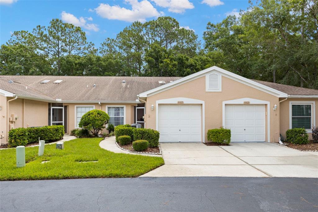 A tan, single-story duplex with two white garage doors and a shared concrete driveway — 4405 CONNERY COURT, PALM HARBOR, FL