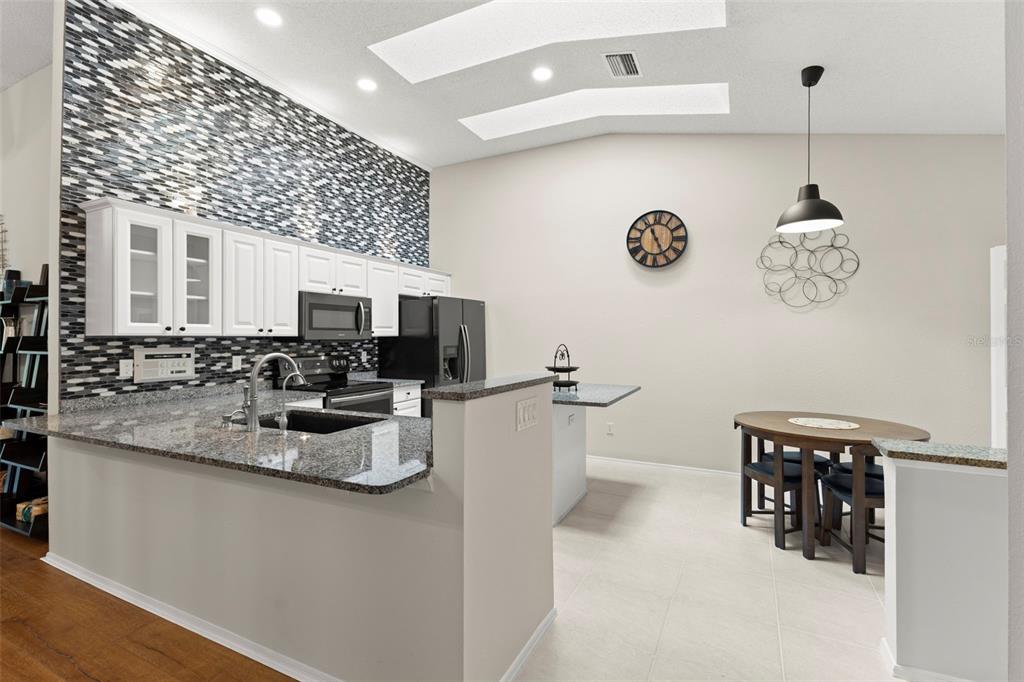 A kitchen with white cabinets, granite countertops, and a mosaic tile backsplash opens to a dining area — 4405 CONNERY COURT, PALM HARBOR, FL