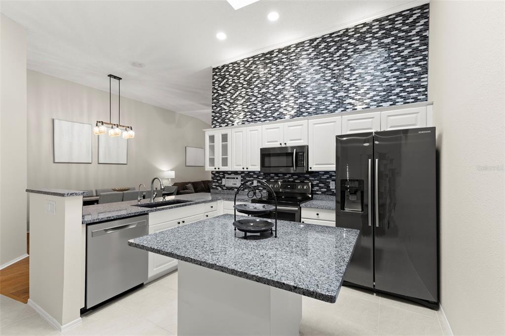 A kitchen features white cabinets, granite countertops, a central island, and a mosaic tile backsplash — 4405 CONNERY COURT, PALM HARBOR, FL