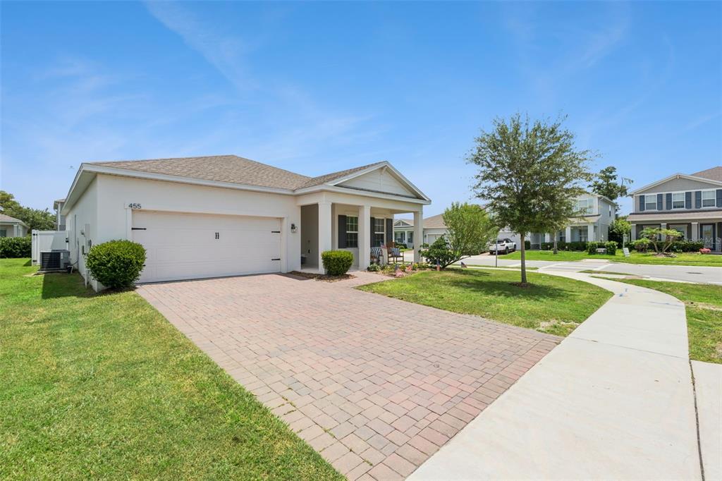 A single-story house with a white exterior, a two-car garage, and a brick paver driveway — 455 WINTER SOLSTICE LANE, MOUNT DORA, FL