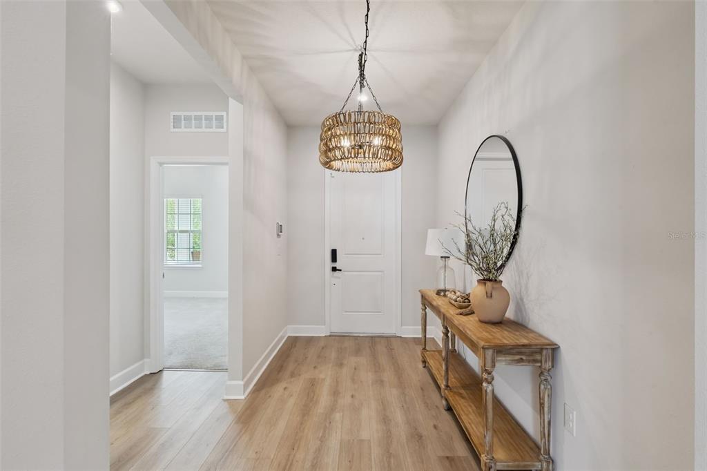 A bright entryway features light wood flooring, a wooden chandelier, and a console table — 455 WINTER SOLSTICE LANE, MOUNT DORA, FL