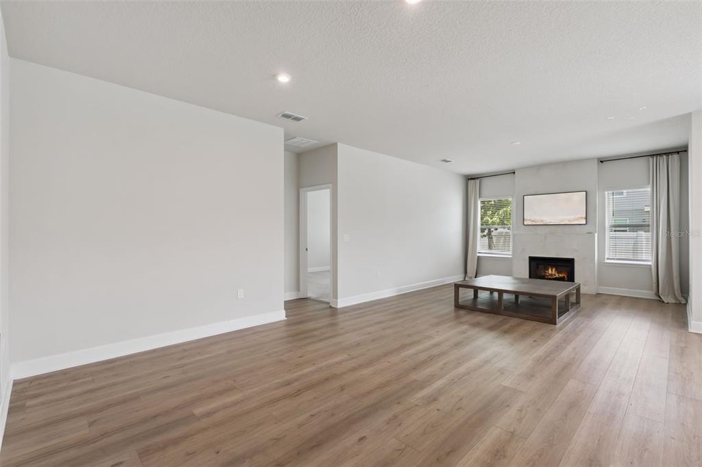 A living room features light wood-look flooring, a fireplace with a marble surround, and windows — 455 WINTER SOLSTICE LANE, MOUNT DORA, FL