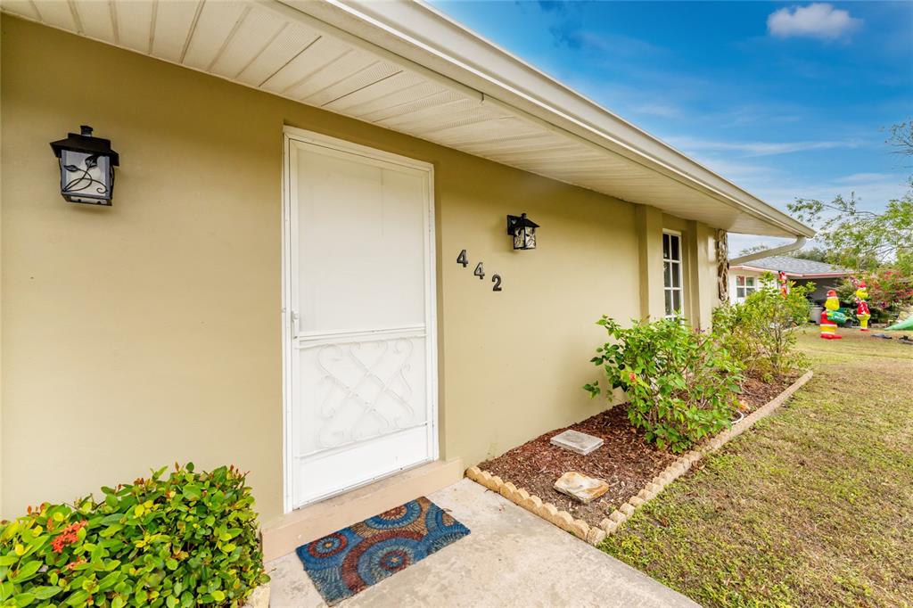 The exterior of a house features a tan wall, a white door, and a walkway — 442 KOSTNER STREET, PORT CHARLOTTE, FL