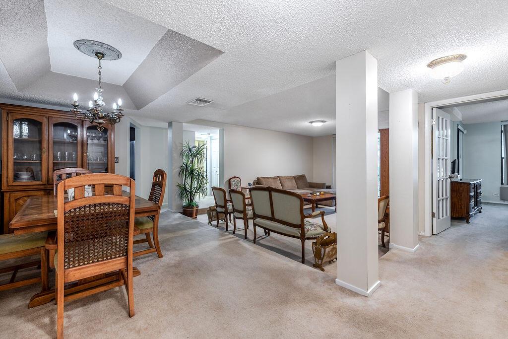 A dining area with a wooden hutch and chairs opens into a living room with carpet — 3680 Inverrary Drive # 1v, Lauderhill FL 33319, LAUDERHILL, FL