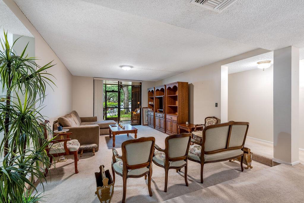 A living room features beige carpet, a brown sectional, wooden shelving, and several vintage chairs — 3680 Inverrary Drive # 1v, Lauderhill FL 33319, LAUDERHILL, FL
