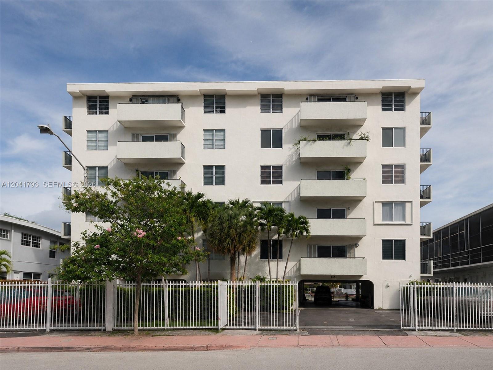 A multi-story white apartment building features balconies, palm trees, and a gated parking entrance — 8024 Tatum Waterway Dr # 6B, Miami Beach FL 33141, MIAMI BEACH, FL