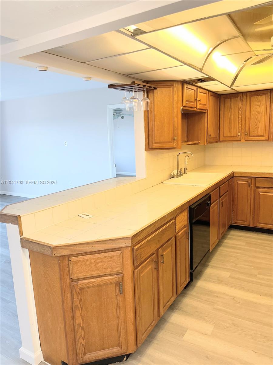 A kitchen features oak cabinets, tiled countertops, and a pass-through window to an adjacent room — 8024 Tatum Waterway Dr # 6B, Miami Beach FL 33141, MIAMI BEACH, FL