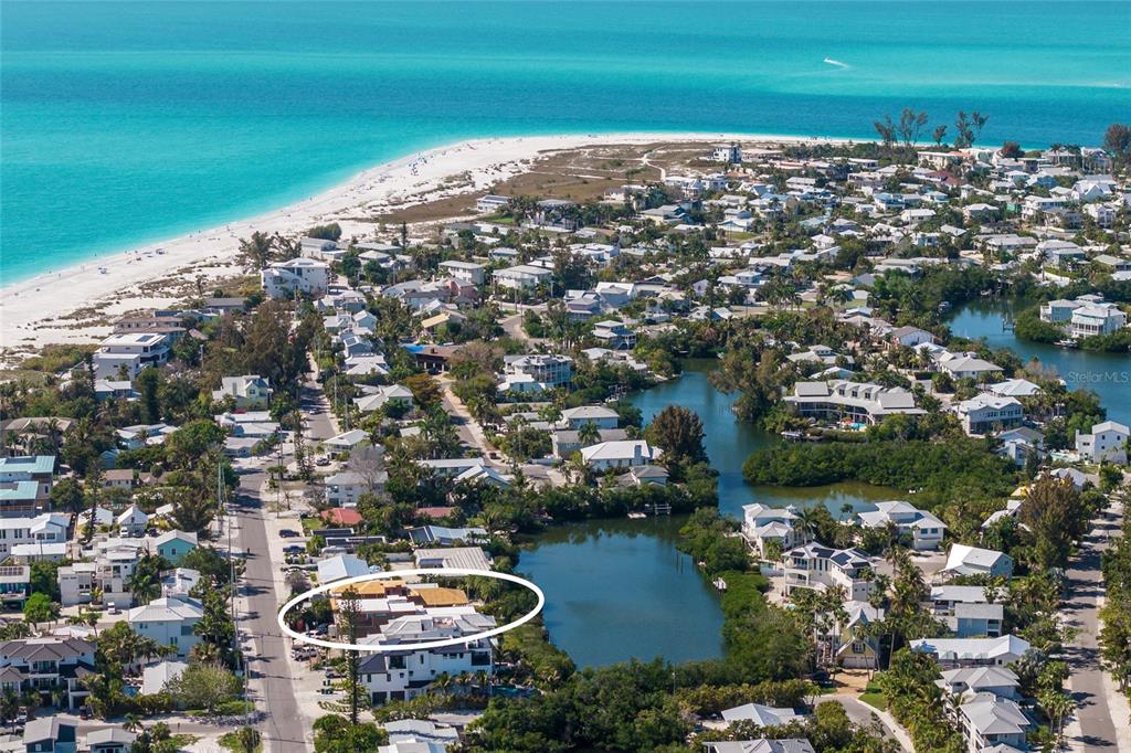An aerial view shows a coastal neighborhood with a white-circled house near a small lake — 406 N SHORE DRIVE, ANNA MARIA, FL
