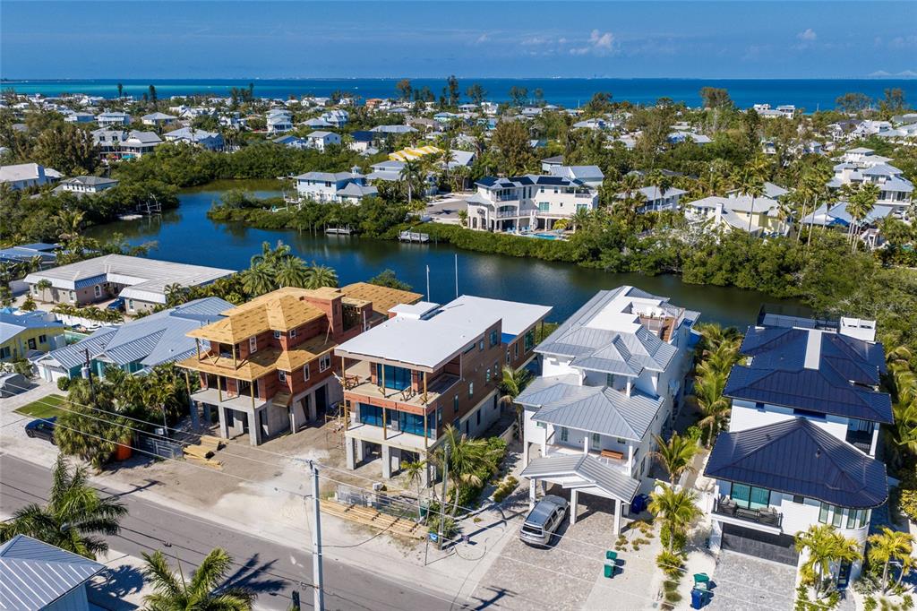 An aerial view shows several coastal homes, including two under construction, near a canal and ocean — 406 N SHORE DRIVE, ANNA MARIA, FL