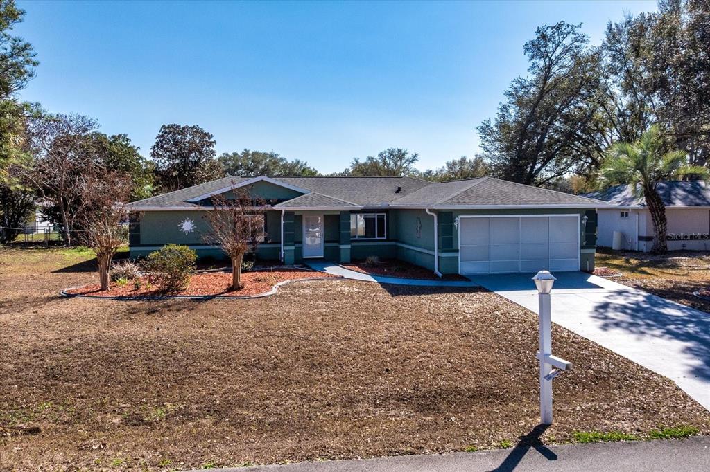A single-story green house with a two-car garage and a paved driveway — 6114 SW 104TH STREET, OCALA, FL
