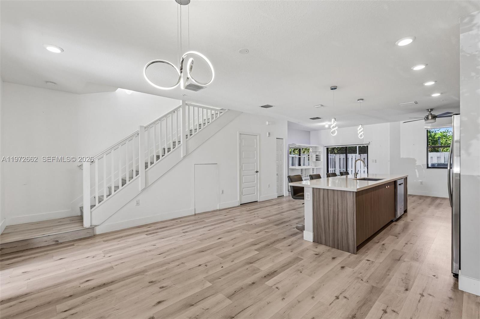 A modern kitchen features a wood-toned island, light flooring, and a staircase with white railings — 10455 NW 82nd St # 4, Doral FL 33178, DORAL, FL