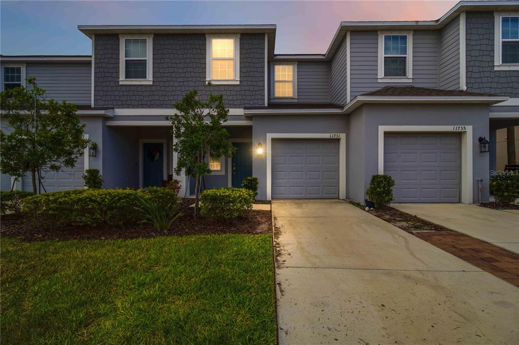 A two-story townhouse exterior features gray siding, two garage doors, and a concrete driveway — 11731 GLENSIDE TERRACE, PALMETTO, FL