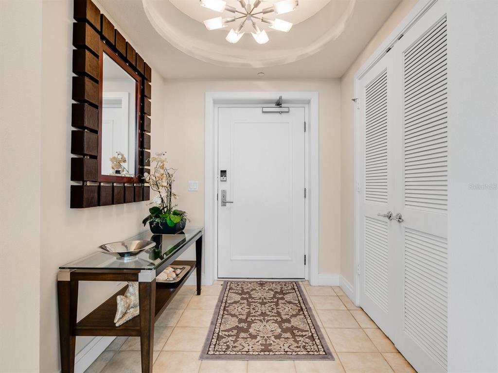 An entryway features a glass-topped console table, a decorative mirror, and a white front door — 6512 MIDNIGHT PASS ROAD UNIT 303, SARASOTA, FL