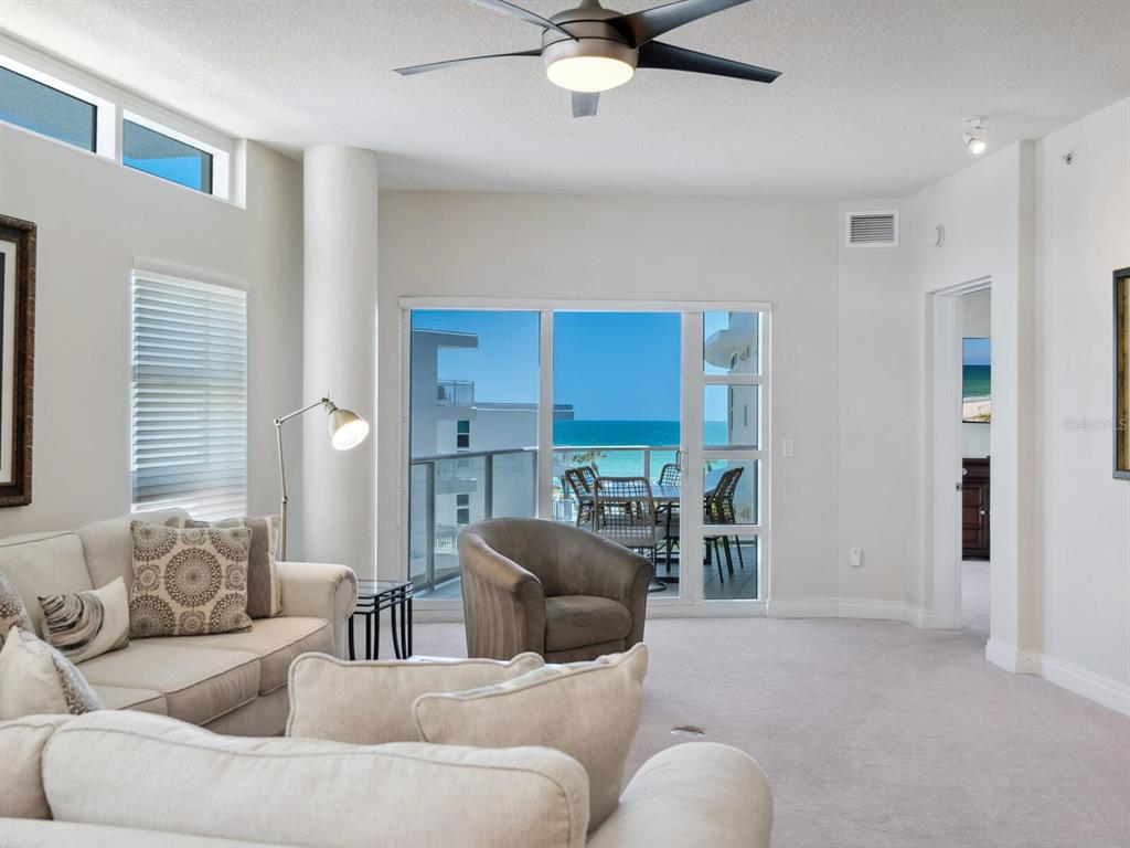 A living room with a ceiling fan, beige furniture, and a sliding door overlooking the ocean — 6512 MIDNIGHT PASS ROAD UNIT 303, SARASOTA, FL